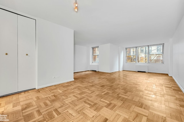 unfurnished living room with radiator heating unit and light parquet flooring