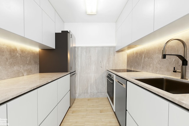 kitchen featuring modern cabinets, a sink, light stone counters, white cabinetry, and stainless steel appliances