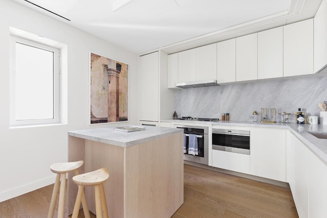 kitchen with backsplash, appliances with stainless steel finishes, white cabinets, and light hardwood / wood-style flooring