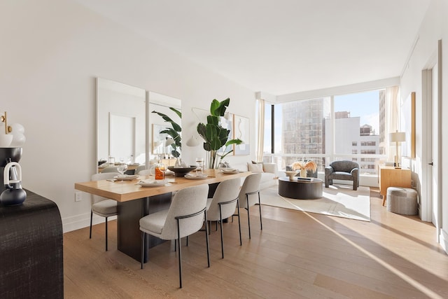 dining room featuring a wall of windows, a view of city, baseboards, and wood finished floors