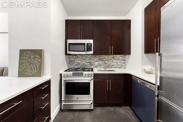 kitchen featuring sink, dark brown cabinets, appliances with stainless steel finishes, dark tile patterned floors, and backsplash