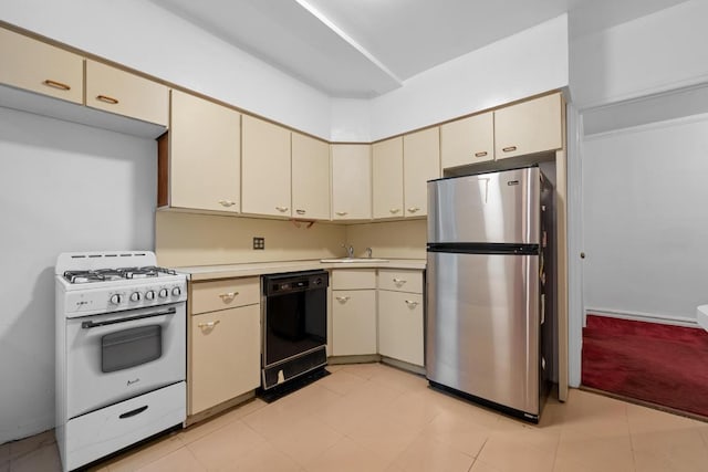 kitchen with black dishwasher, light countertops, cream cabinets, freestanding refrigerator, and white gas range oven