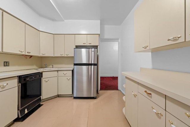 kitchen with dishwasher, freestanding refrigerator, light countertops, cream cabinetry, and a sink