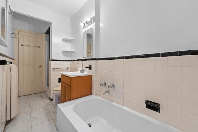 bathroom featuring tile walls, toilet, marble finish floor, vanity, and a bath