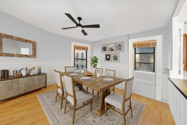 dining area featuring ceiling fan, light wood finished floors, and wainscoting