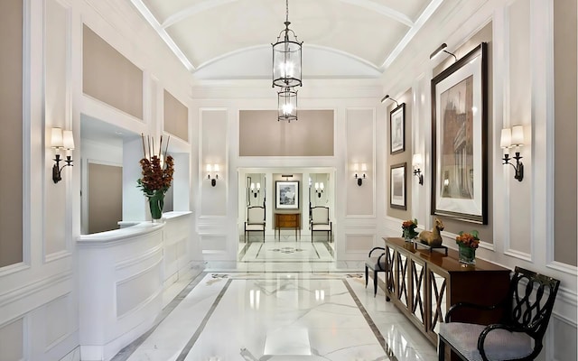 corridor featuring lofted ceiling, marble finish floor, a chandelier, and a decorative wall