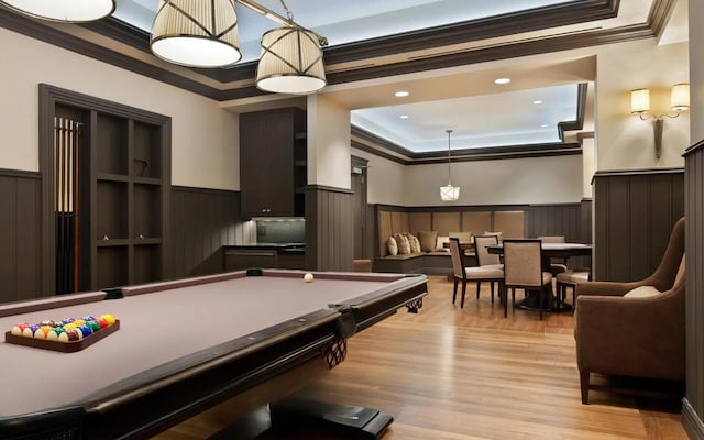 recreation room with a tray ceiling, a wainscoted wall, recessed lighting, light wood-style flooring, and ornamental molding