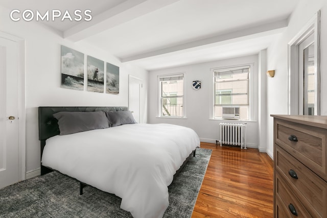 bedroom featuring beam ceiling, baseboards, radiator heating unit, and wood finished floors