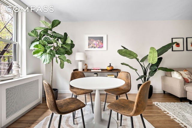 dining space with radiator heating unit, baseboards, and wood finished floors