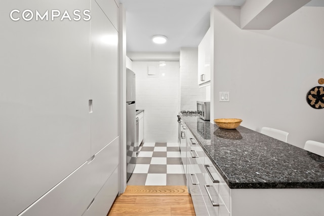 kitchen featuring freestanding refrigerator, dark stone counters, a peninsula, white cabinets, and light floors