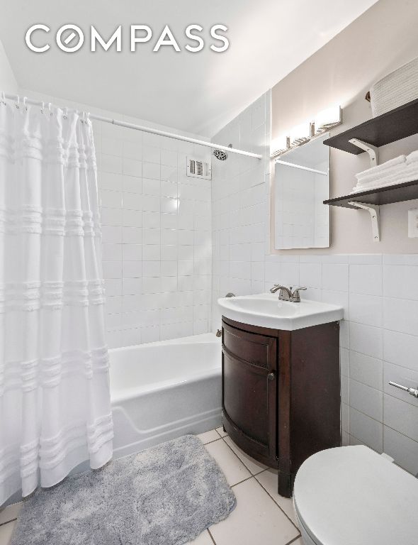 full bathroom featuring shower / bathtub combination with curtain, tile walls, vanity, tile patterned floors, and toilet