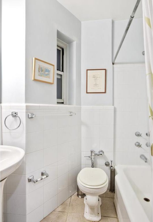 bathroom featuring tile patterned flooring, tile walls, shower / tub combo with curtain, and toilet