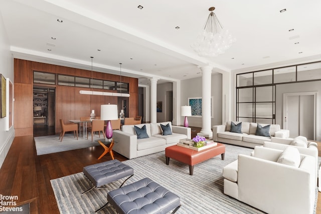 living room featuring ornate columns, wood-type flooring, a chandelier, expansive windows, and wood walls