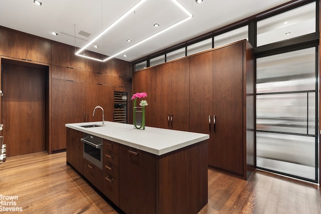 kitchen featuring dark wood-type flooring, sink, wood walls, a kitchen island with sink, and oven