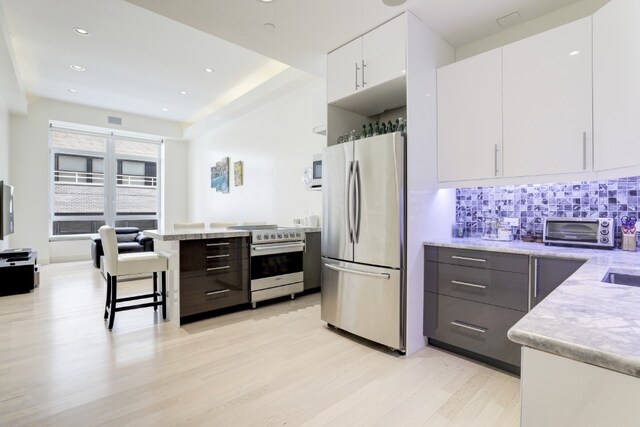 kitchen with appliances with stainless steel finishes, tasteful backsplash, white cabinetry, a kitchen breakfast bar, and light stone countertops