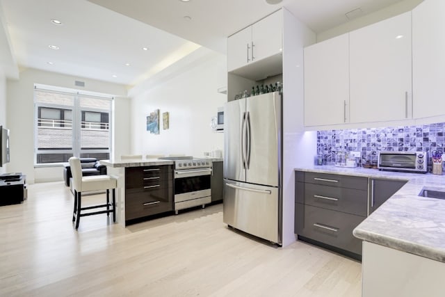 kitchen featuring a kitchen bar, backsplash, stainless steel appliances, white cabinets, and light stone countertops