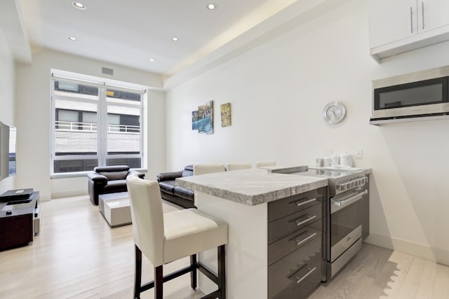 kitchen with light wood-type flooring, dark brown cabinets, stainless steel appliances, and a breakfast bar area