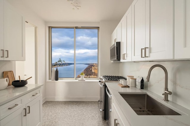 kitchen featuring appliances with stainless steel finishes, white cabinets, light stone counters, and sink