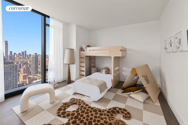 bedroom featuring baseboards, floor to ceiling windows, a city view, and wood finished floors