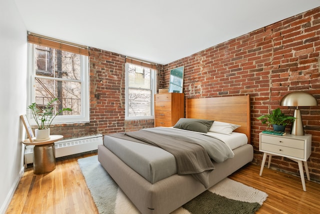bedroom with brick wall, baseboards, and hardwood / wood-style flooring