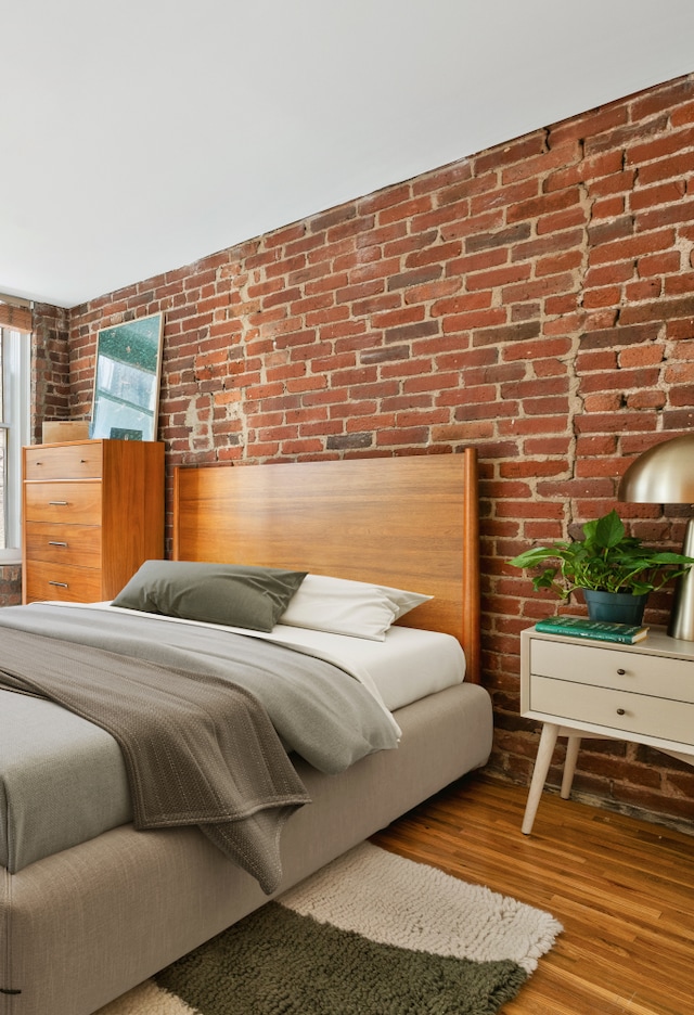bedroom with wood finished floors and brick wall