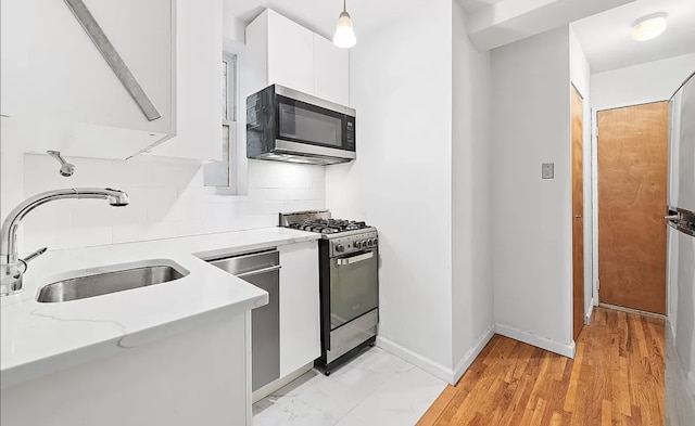 kitchen with backsplash, light stone countertops, a sink, stainless steel appliances, and white cabinetry