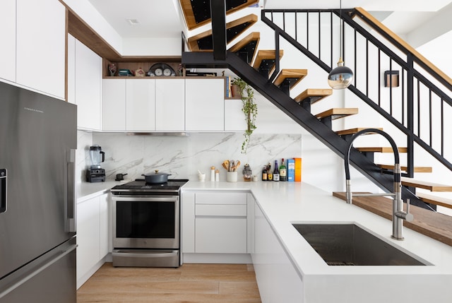 kitchen featuring white cabinets, decorative backsplash, stainless steel appliances, light countertops, and a sink