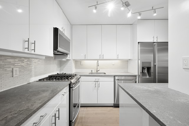 16 W 16th St Unit 8Rs, New York City, NY 10011 - kitchen with stainless steel appliances, dark stone countertops, backsplash, white cabinetry, and rail lighting