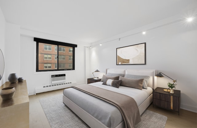 bedroom with light wood-type flooring, track lighting, an AC wall unit, and baseboard heating