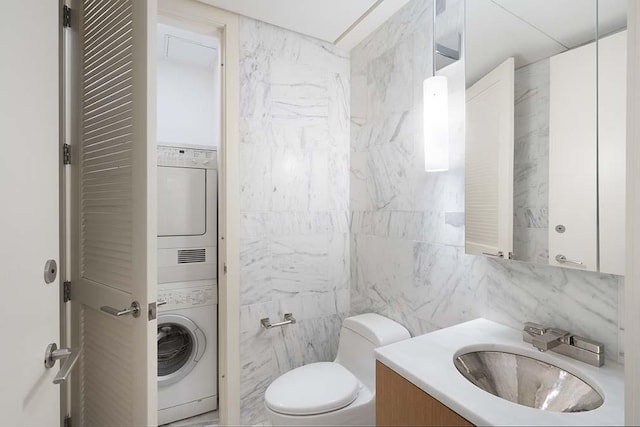 bathroom with stacked washing maching and dryer, tile walls, vanity, and toilet