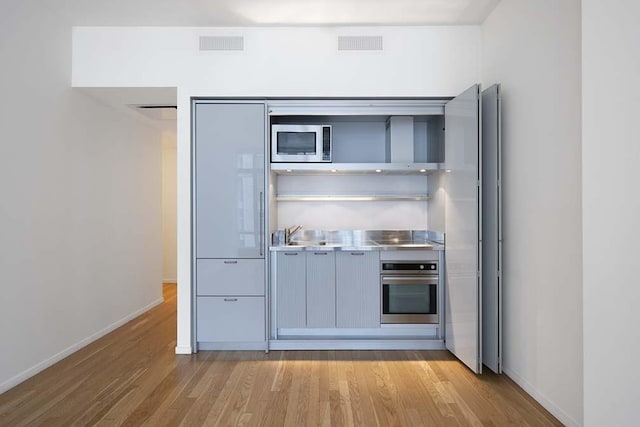 kitchen with sink, light wood-type flooring, stainless steel counters, and appliances with stainless steel finishes