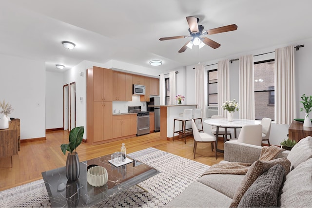 living area featuring a ceiling fan, light wood-type flooring, and baseboards