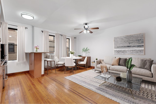 living area featuring a ceiling fan, baseboards, and light wood finished floors