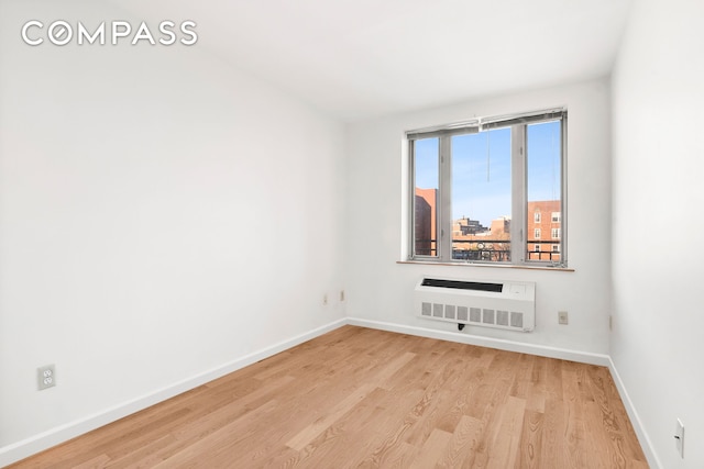 unfurnished room featuring a wall mounted air conditioner, baseboards, wood finished floors, and a view of city