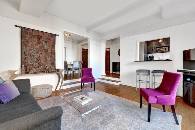 living area featuring beam ceiling, wood finished floors, and baseboards