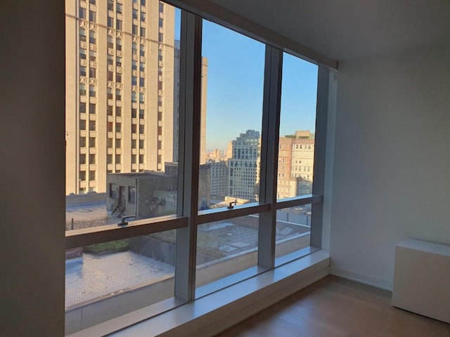 doorway to outside featuring a view of city, expansive windows, wood finished floors, and baseboards