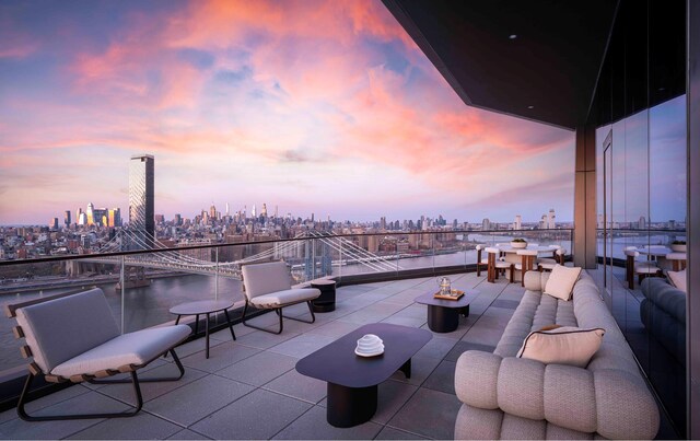 patio terrace at dusk with a view of city, a balcony, and a water view