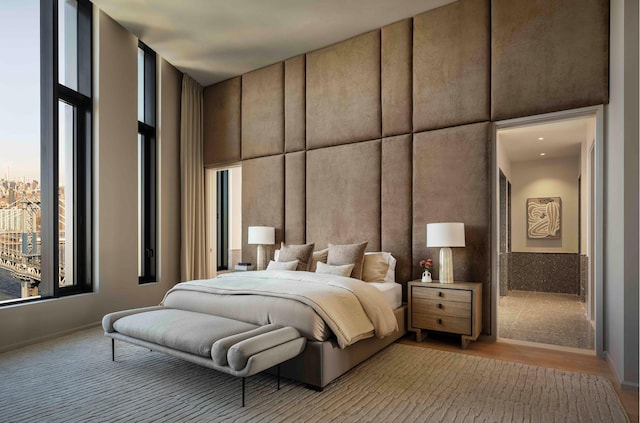 bedroom with a high ceiling, light wood-style flooring, and floor to ceiling windows