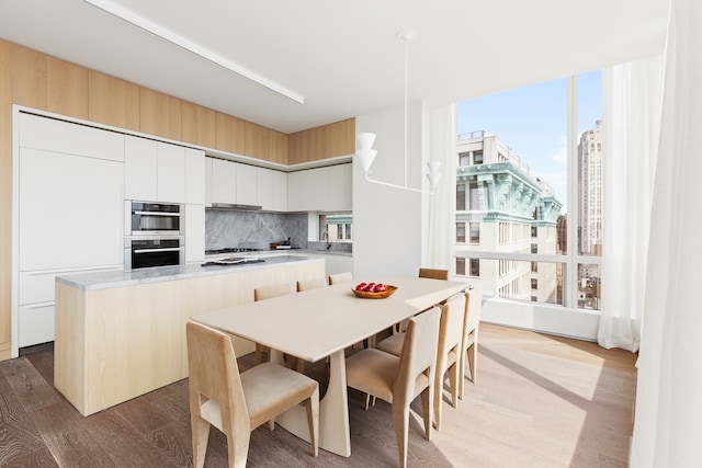 kitchen with stainless steel double oven, white gas stovetop, wood finished floors, a kitchen island, and decorative backsplash