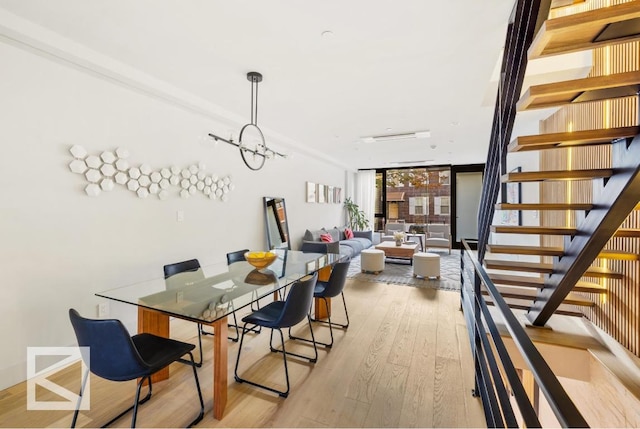 dining space featuring a wall of windows, light wood-type flooring, a notable chandelier, and stairs