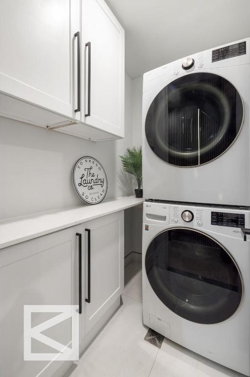 laundry area featuring light tile patterned floors, stacked washer / dryer, and cabinet space