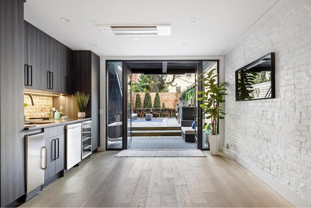 doorway to outside featuring brick wall, wine cooler, a sink, and light wood-style floors