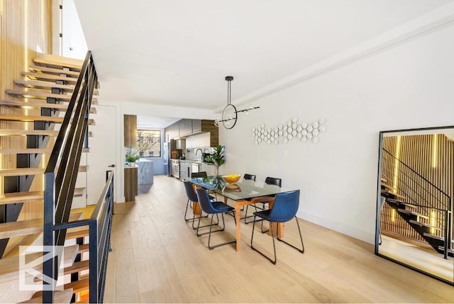 dining area with light wood-style floors, baseboards, an inviting chandelier, and stairs