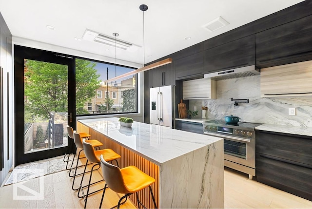 kitchen with stainless steel appliances, a kitchen island, exhaust hood, a kitchen breakfast bar, and decorative light fixtures