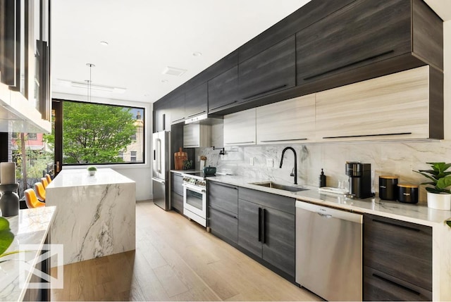 kitchen with light stone counters, high end appliances, tasteful backsplash, a sink, and modern cabinets