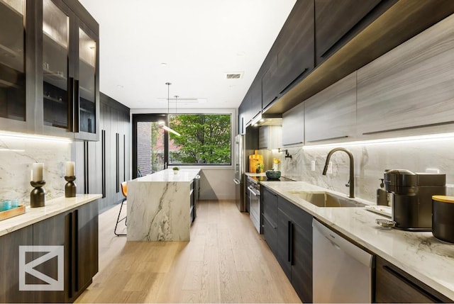 kitchen featuring light stone counters, pendant lighting, appliances with stainless steel finishes, glass insert cabinets, and a sink