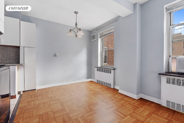 unfurnished dining area with light parquet floors, radiator heating unit, and an inviting chandelier