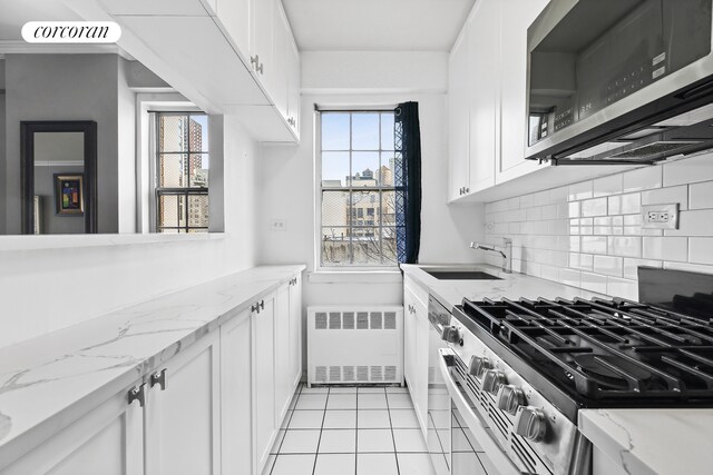 kitchen with appliances with stainless steel finishes, radiator heating unit, white cabinetry, sink, and light stone counters