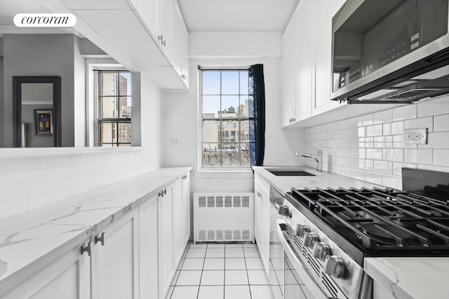 kitchen with white cabinets, appliances with stainless steel finishes, radiator heating unit, sink, and light stone counters