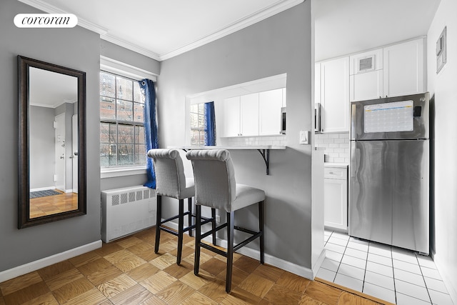 kitchen featuring a breakfast bar, decorative backsplash, radiator heating unit, freestanding refrigerator, and white cabinetry